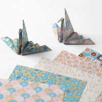 Floral-patterned paper sheets with folded origami cranes on a white background